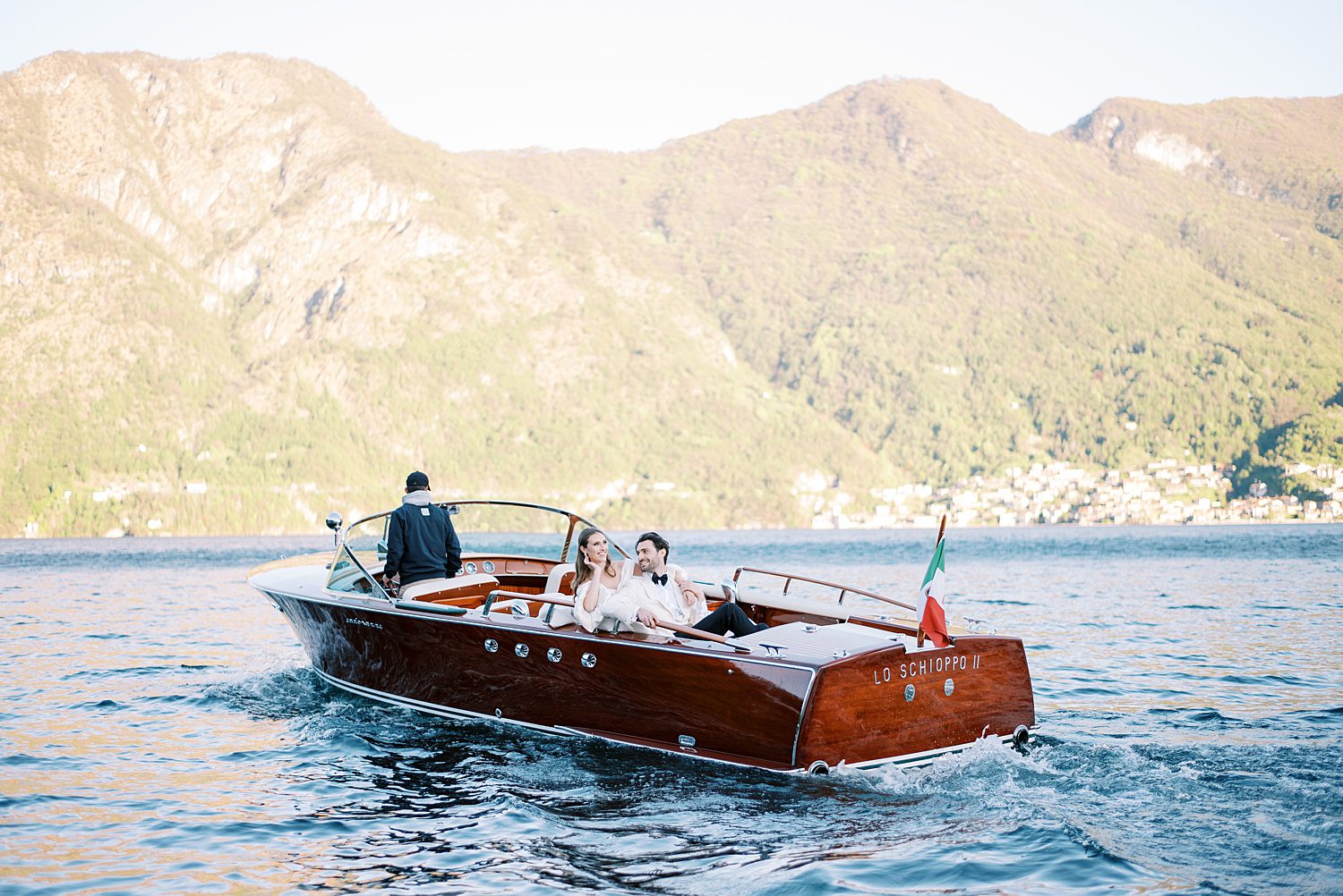 bride and groom sit on red boat on Lake Como in Italy 