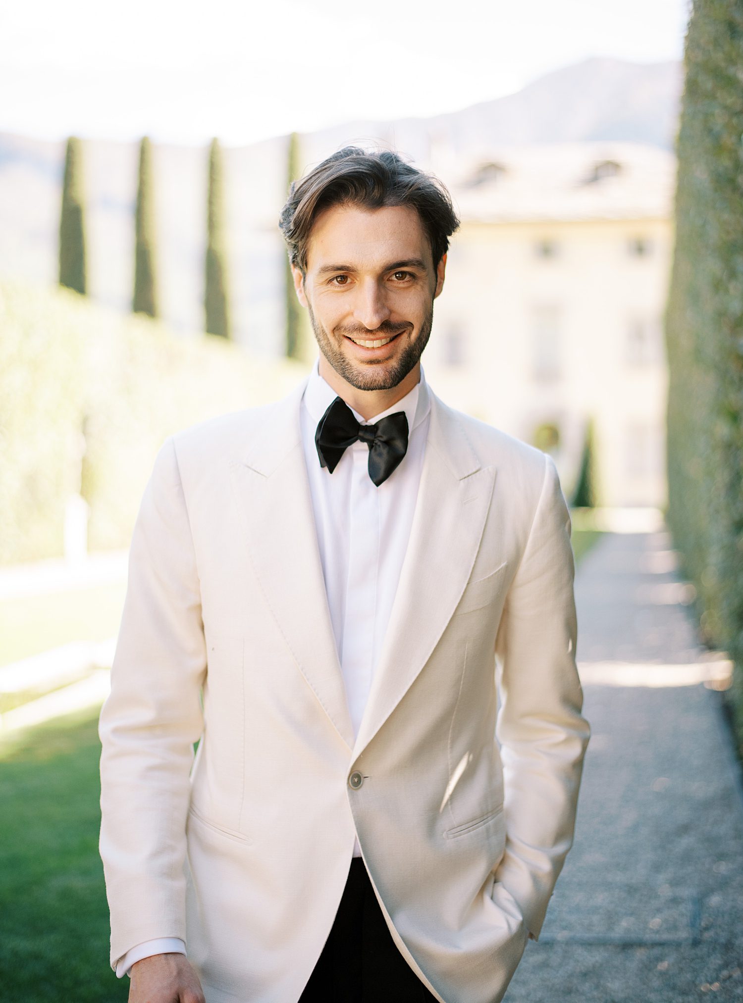 groom stands with hands in pocket of ivory tux