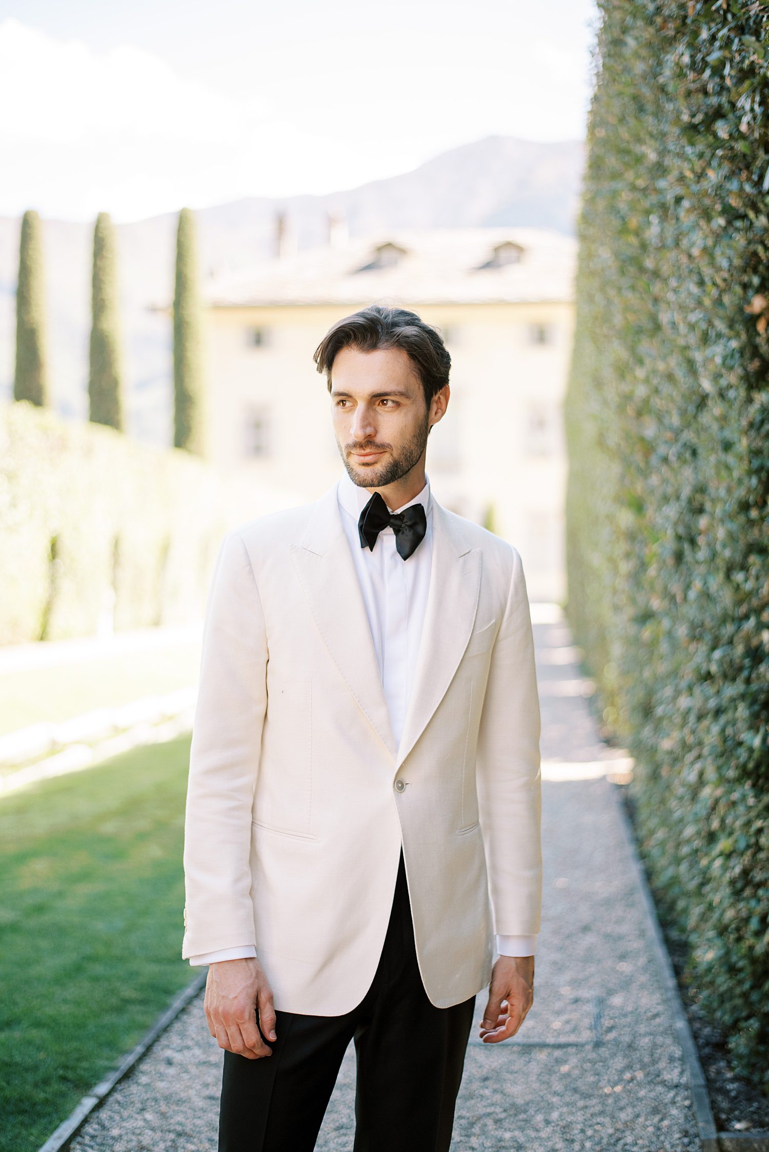 groom stands in ivory tux outside Villa Balbiano