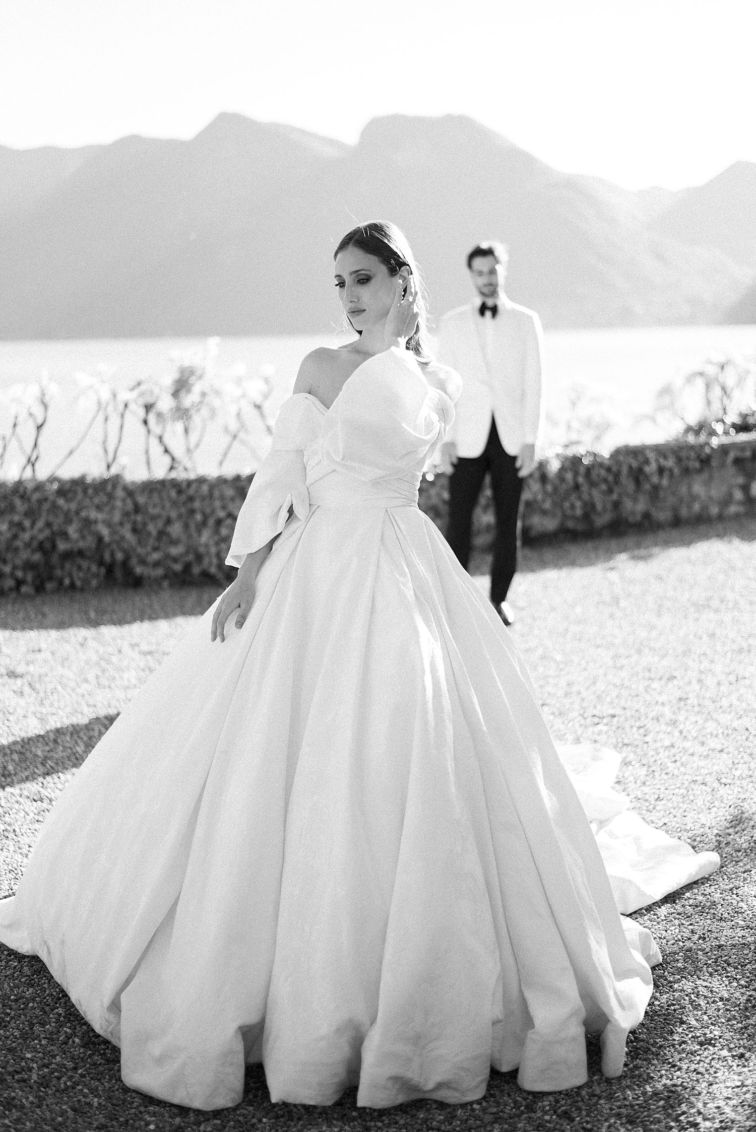bride pushes hair behind ears on lawn in front of Lake Como 