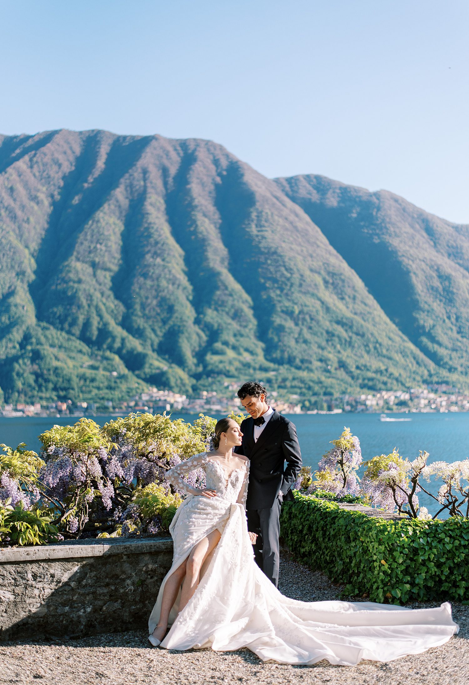 bride sits in front of Lake Como with wedding gown with slit designed by Ines Di Santo