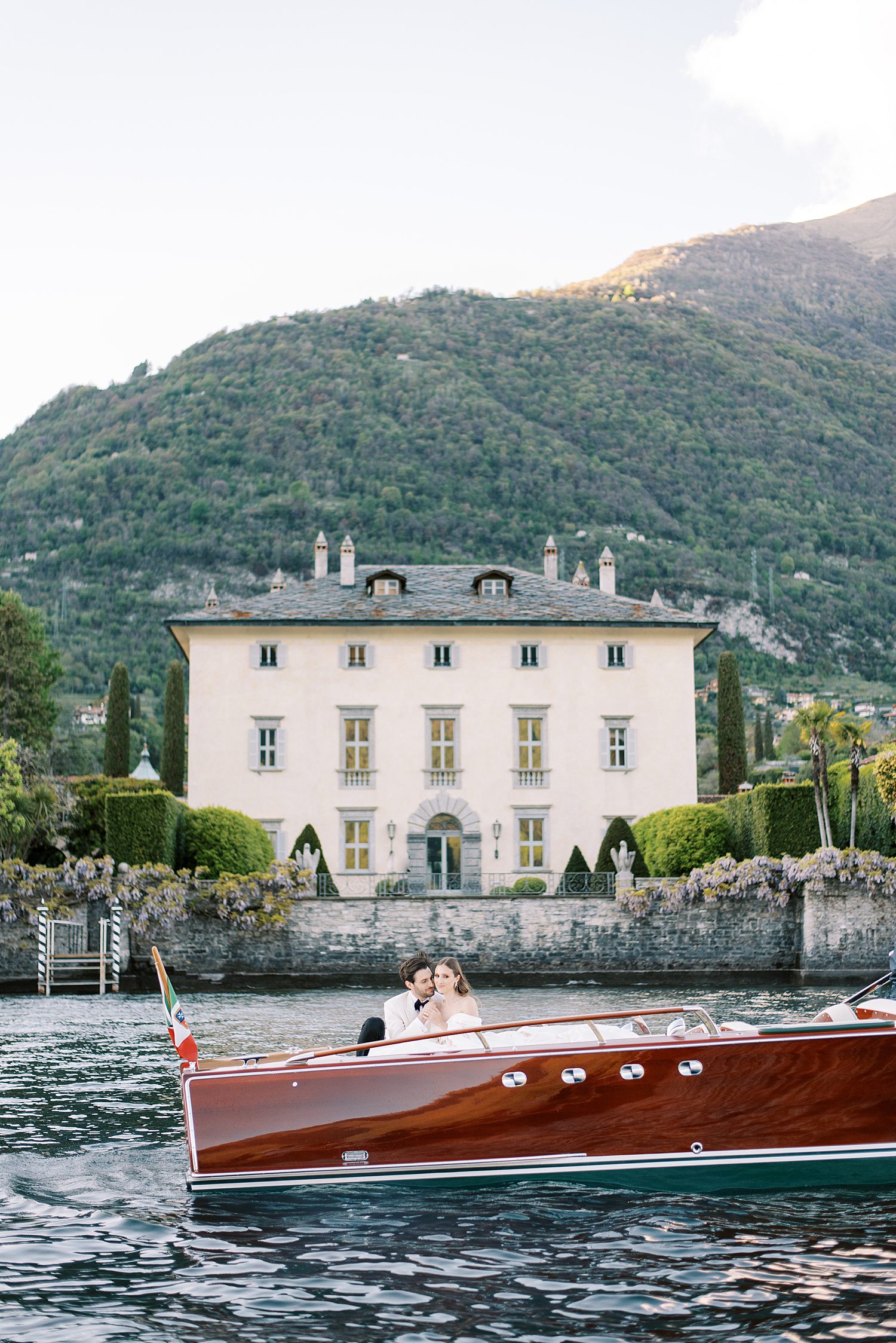 bride and groom ride on red boat in front of Villa Balbiano on Lake Como 