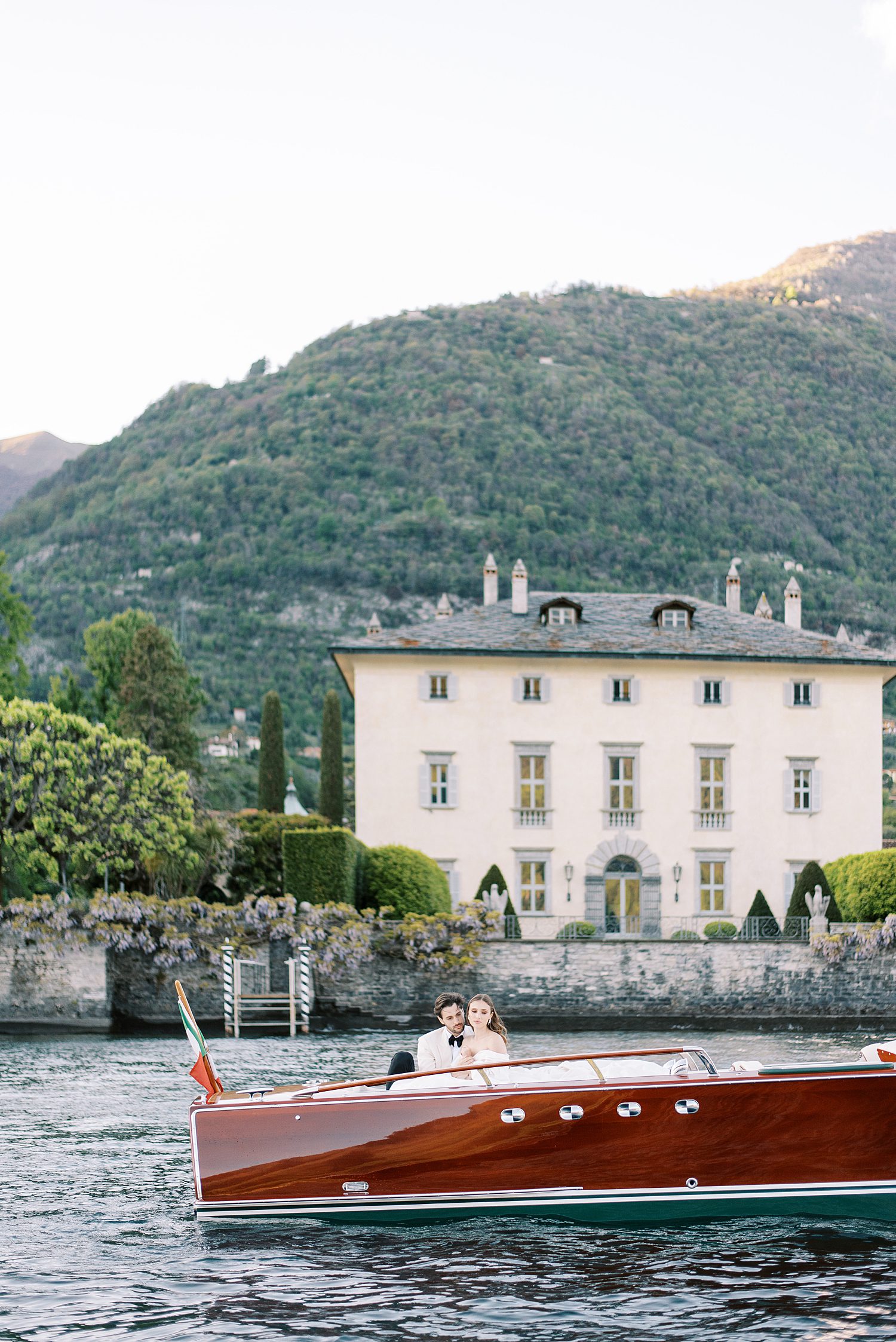 newlyweds ride in red boat in front of Villa Balbiano on Lake Como 
