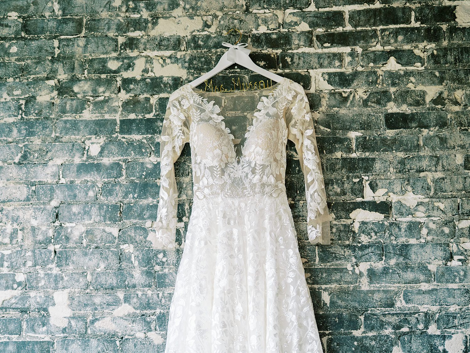 wedding dress with lace sleeves hangs on blue brick inside the Oxford Exchange