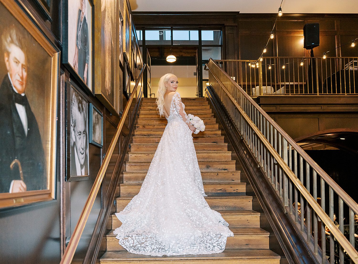bride stands on staircase inside the Oxford Exchange with wedding gown draped down steps