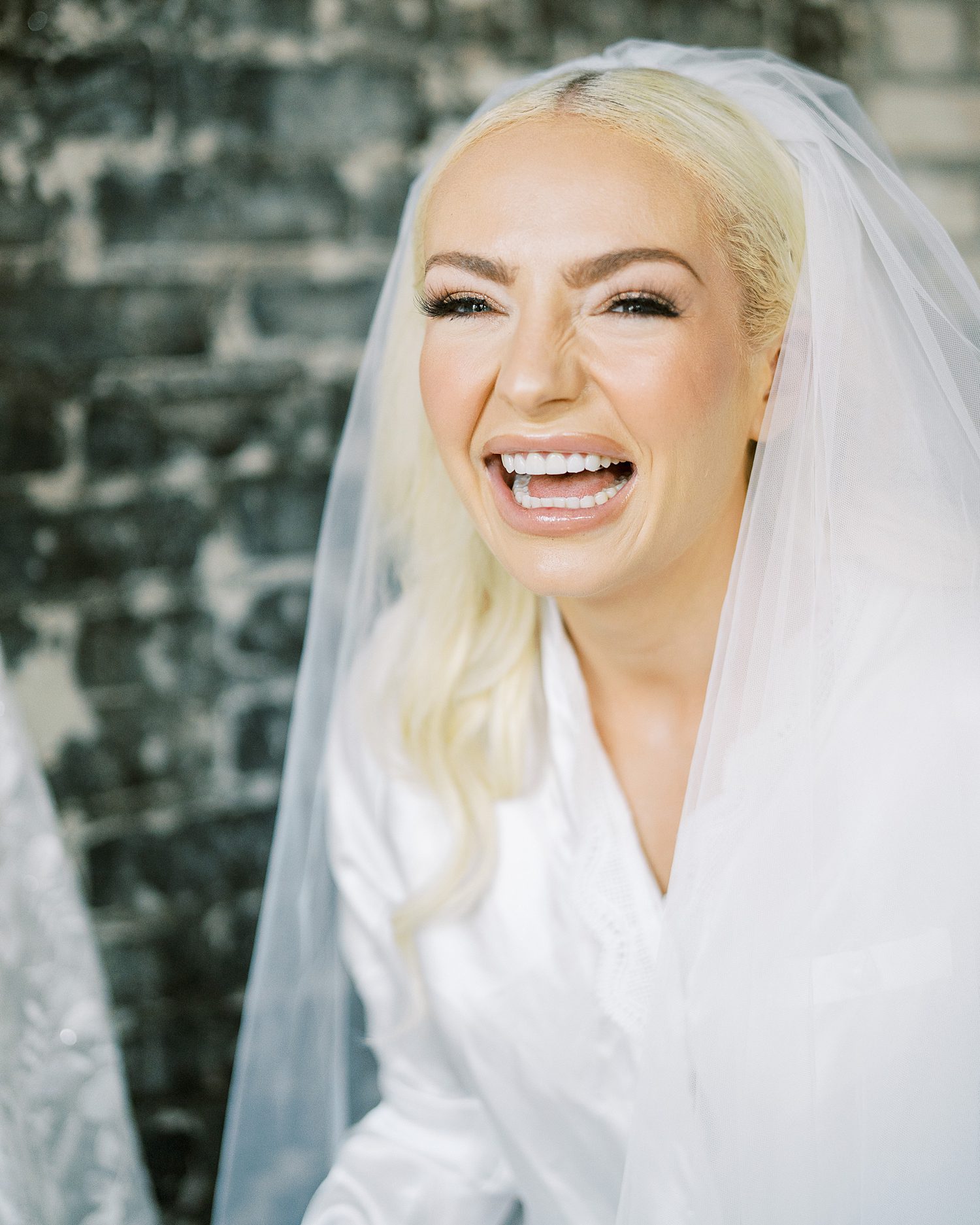 bride laughs in white robe with veil around her shoulders 