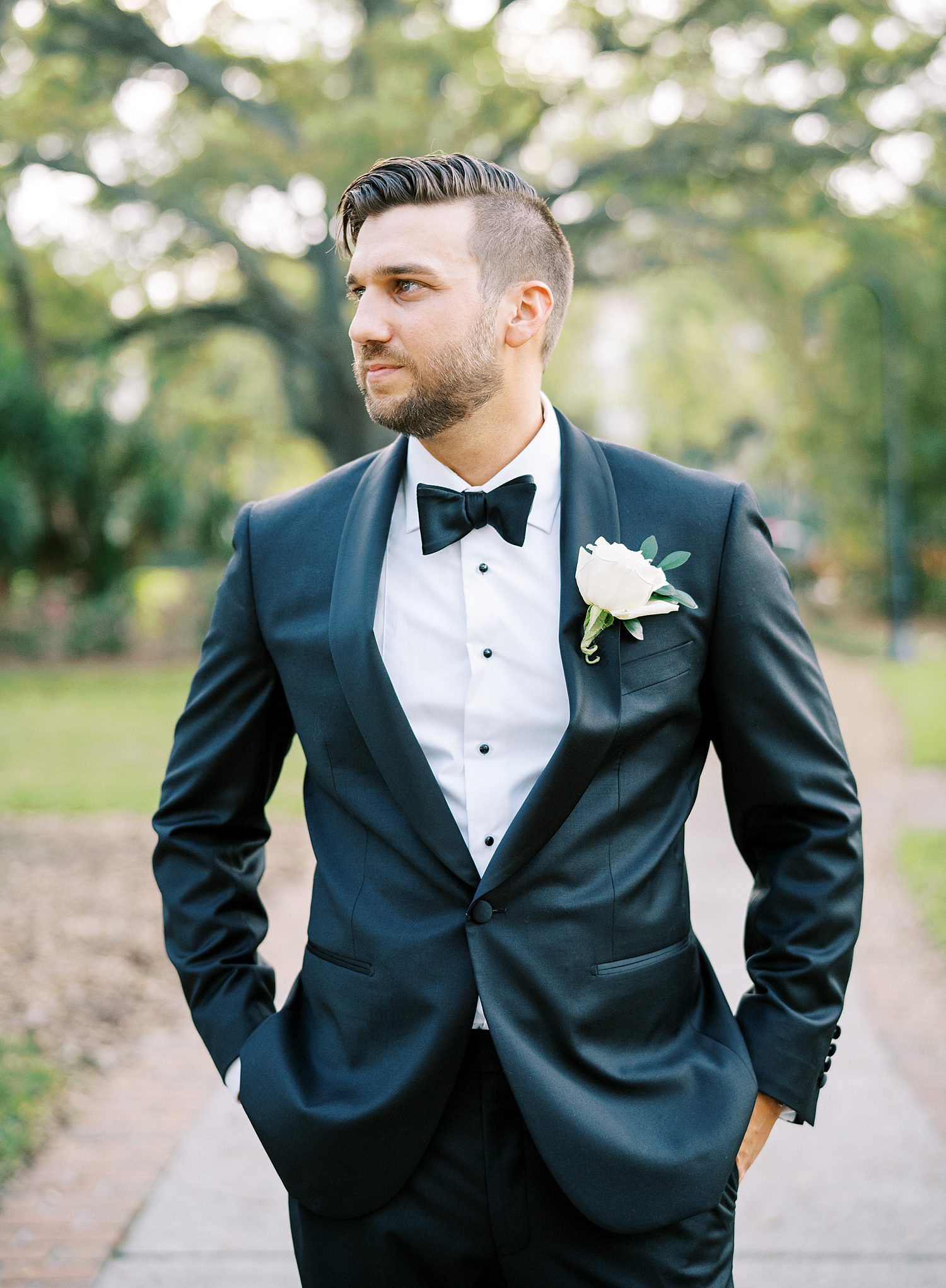 groom stands with hands in pockets of his black tux