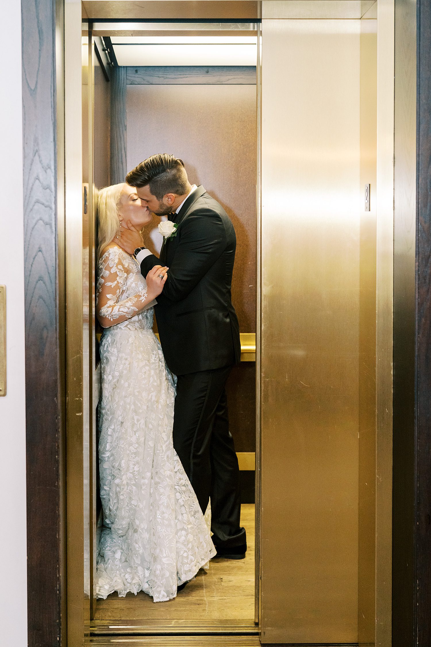 groom leans to kiss bride pushing her against wall of elevator 