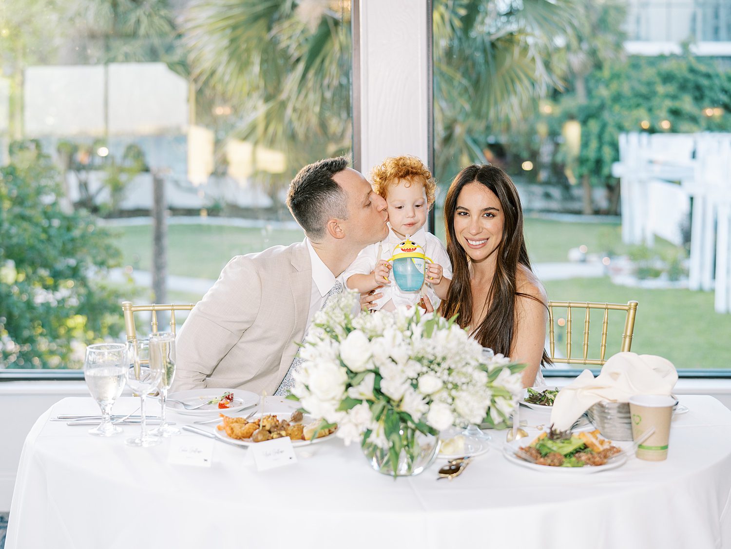 bride and groom sit at sweetheart table with son during reception at the Rusty Pelican Tampa