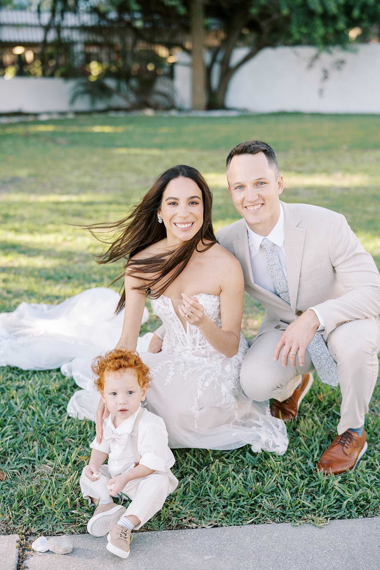 bride and groom kneel with son on grass in Tampa FL