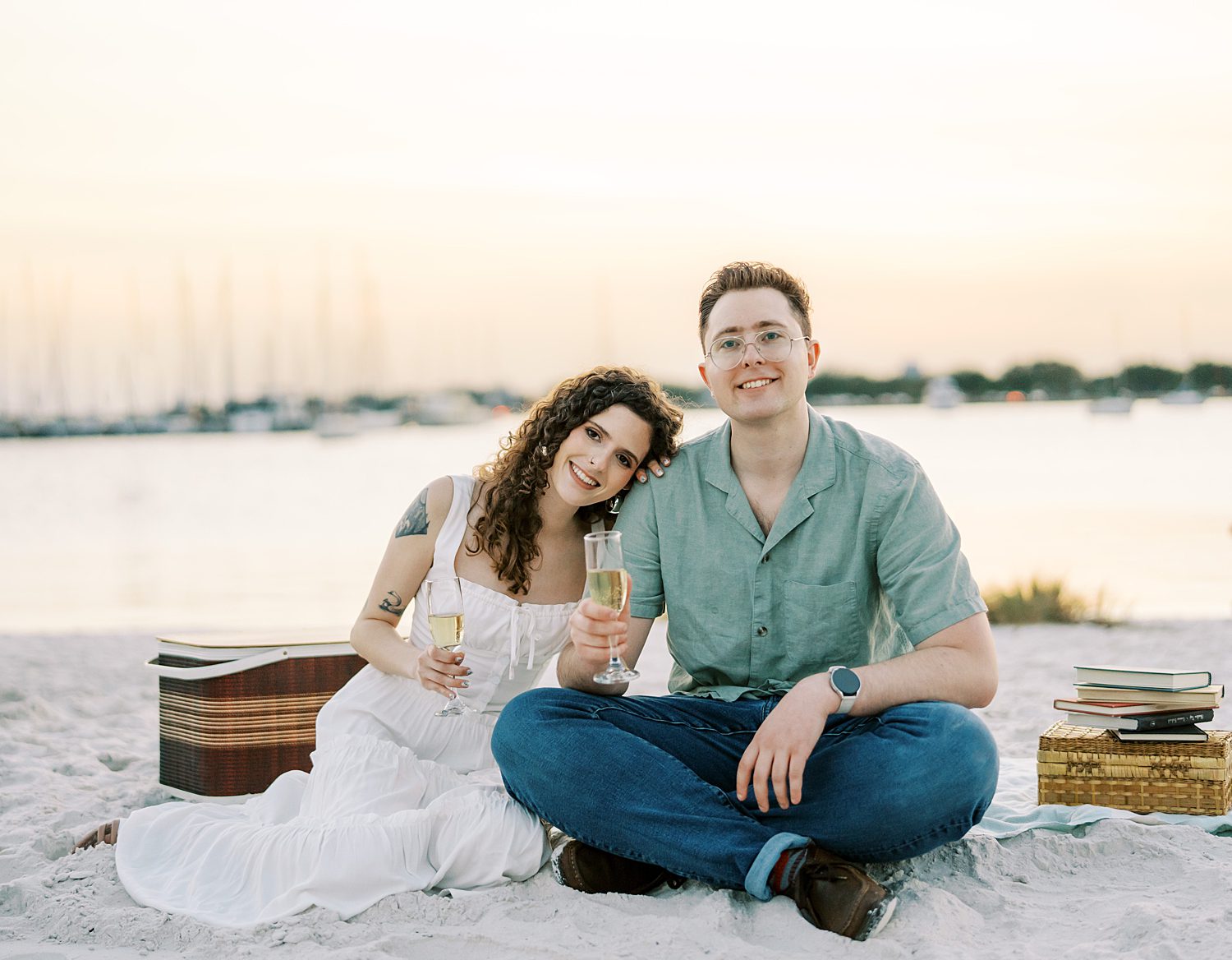 woman sits in white dress holding glass of champagne and leaning head on groom's shoulder