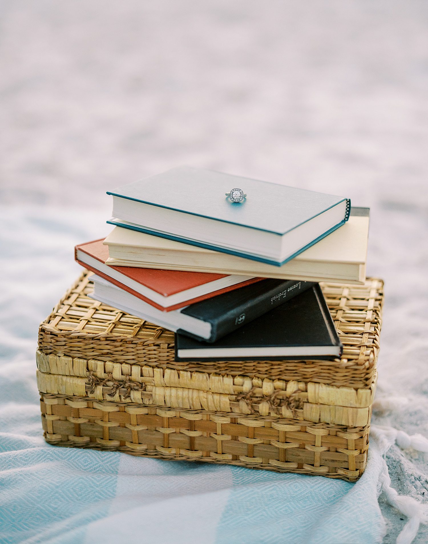 stack of books on wicker basket with engagement ring on top