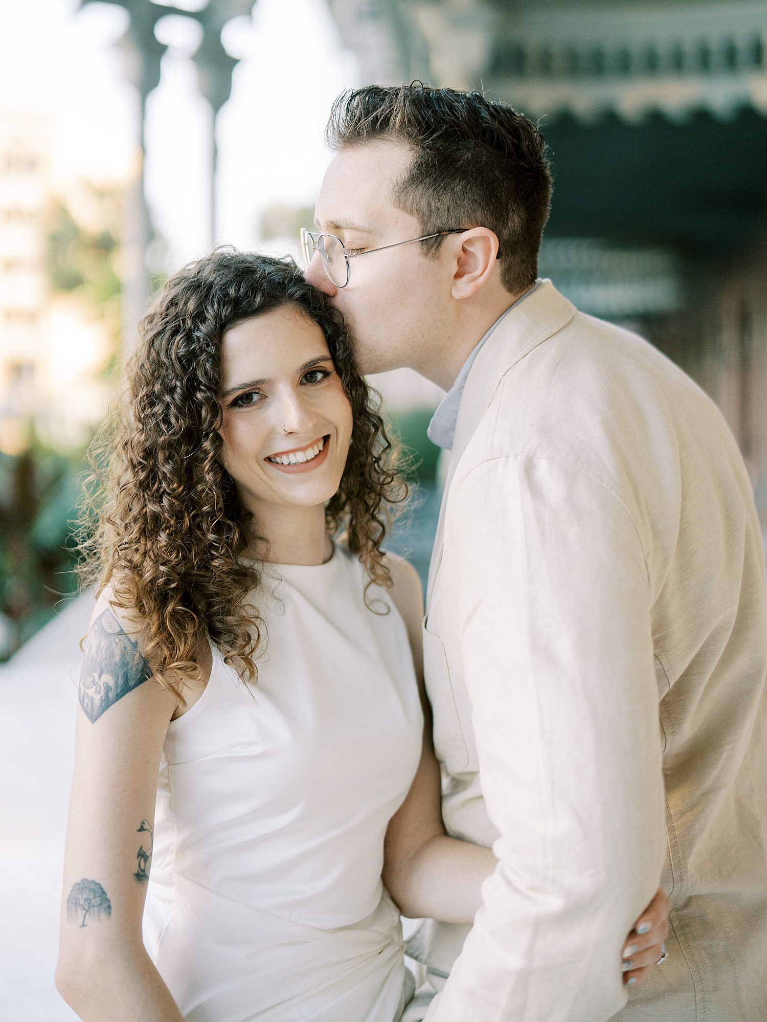 man in tan linen suit kisses woman's head during engagement photos 