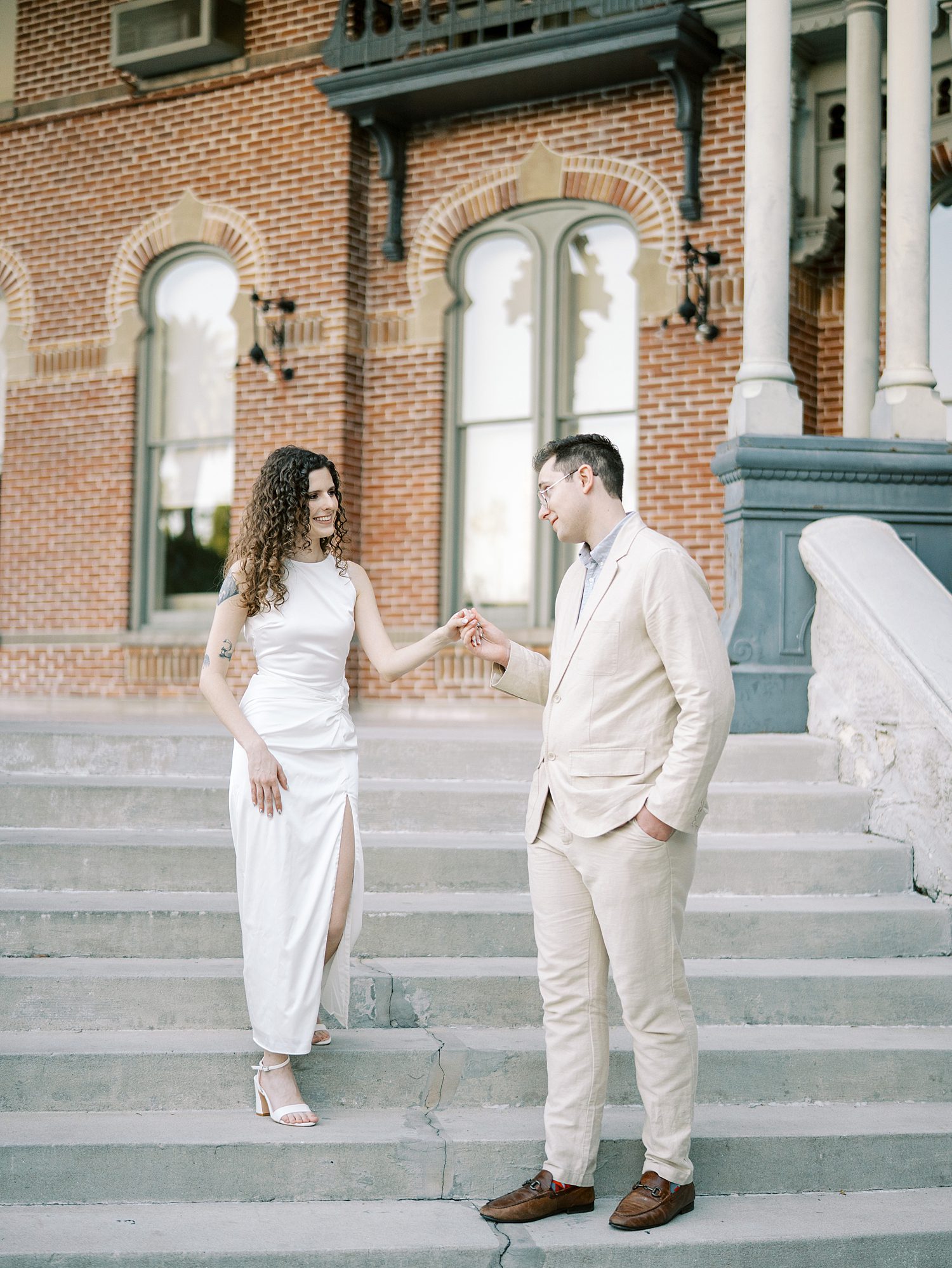 man in tan linen suit helps bride down steps at the University of Tampa