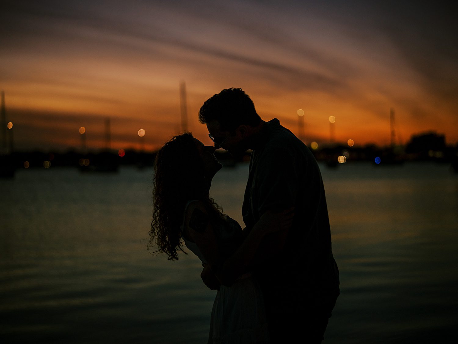 man and woman kiss silhouetted against red and orange sunset on Davis Island beach 