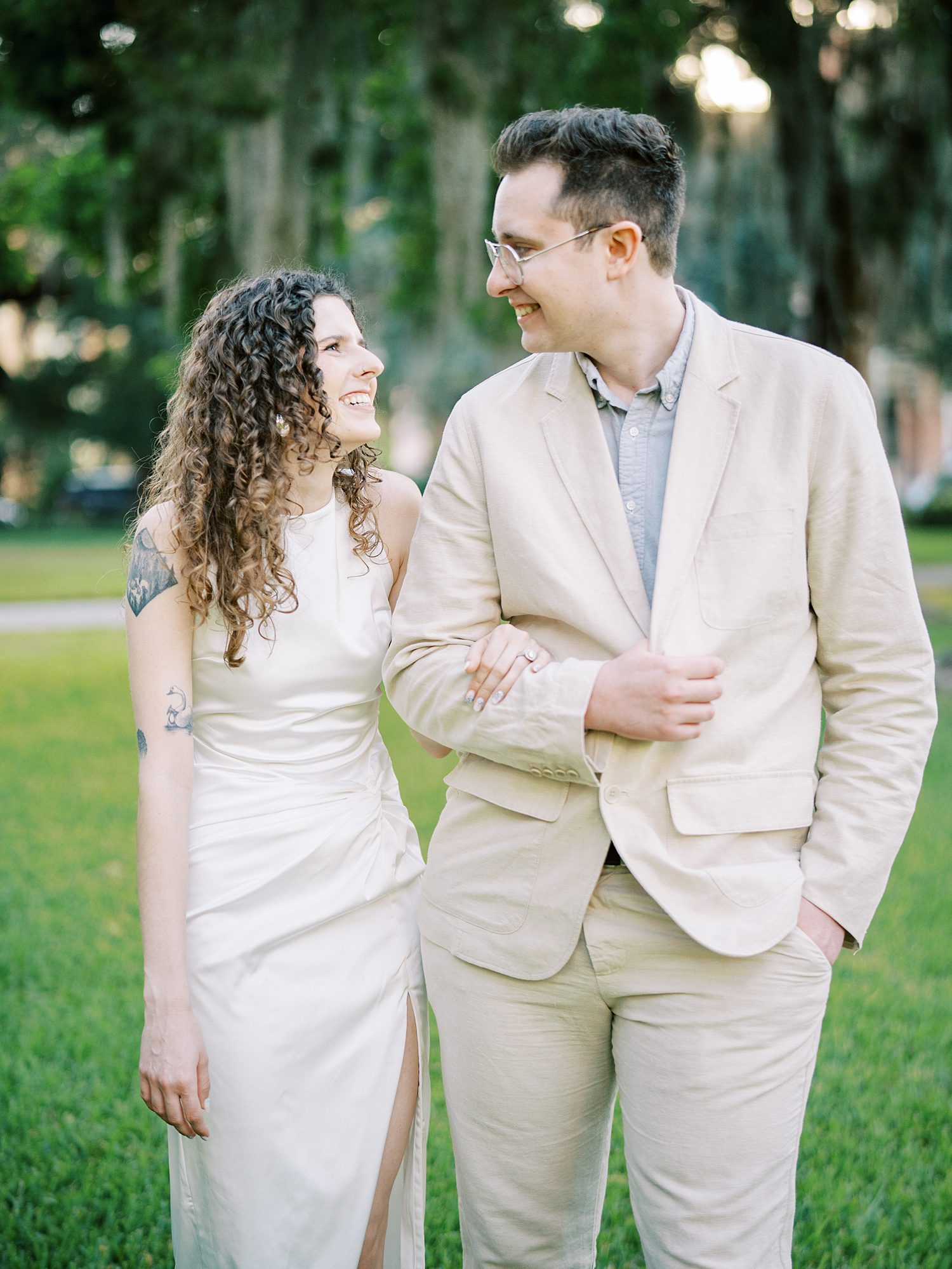 man in tan linen suit escorts woman across lawn on his arm