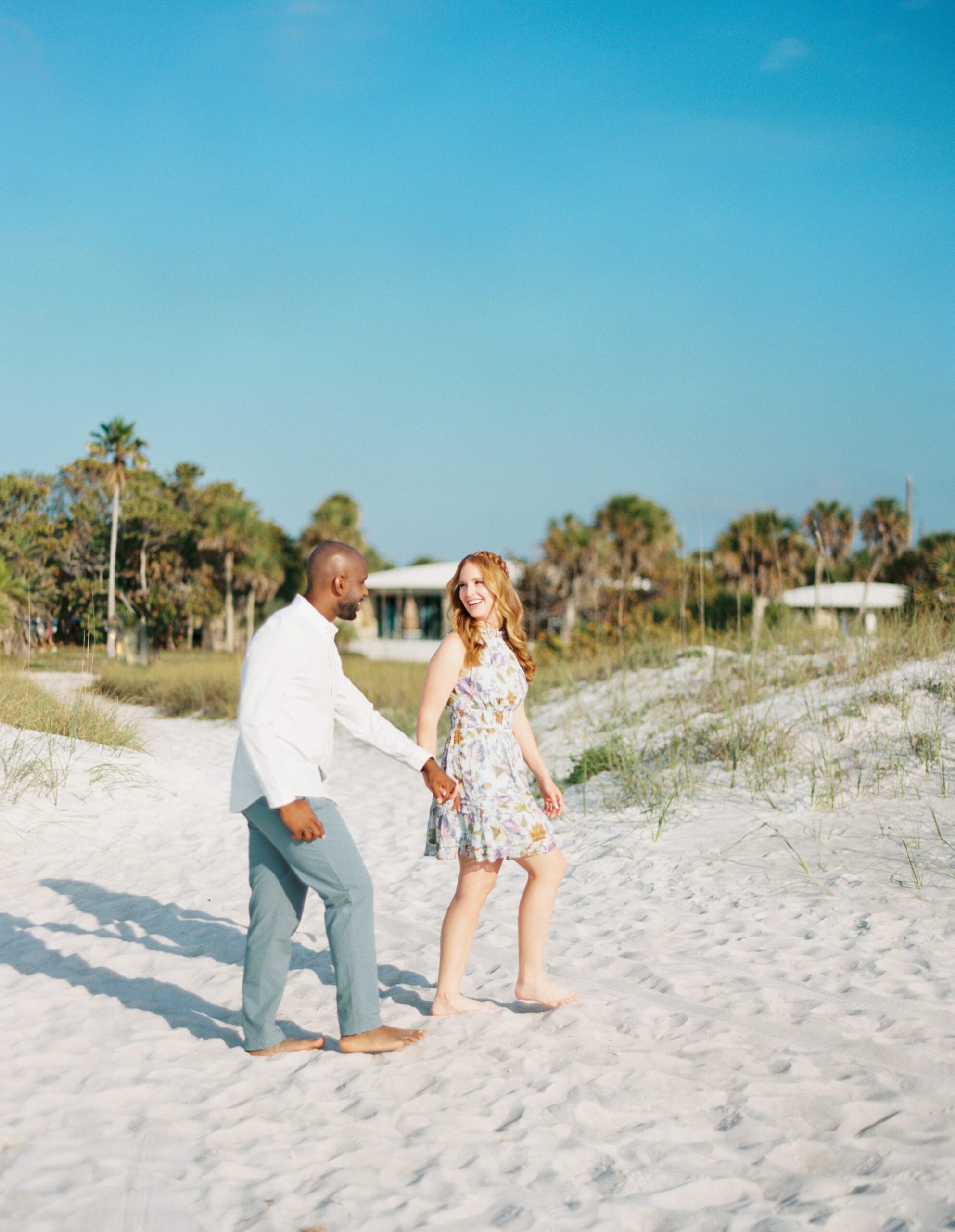 Fort de soto engagement session bride and groom walking on the beach smiling at each other 