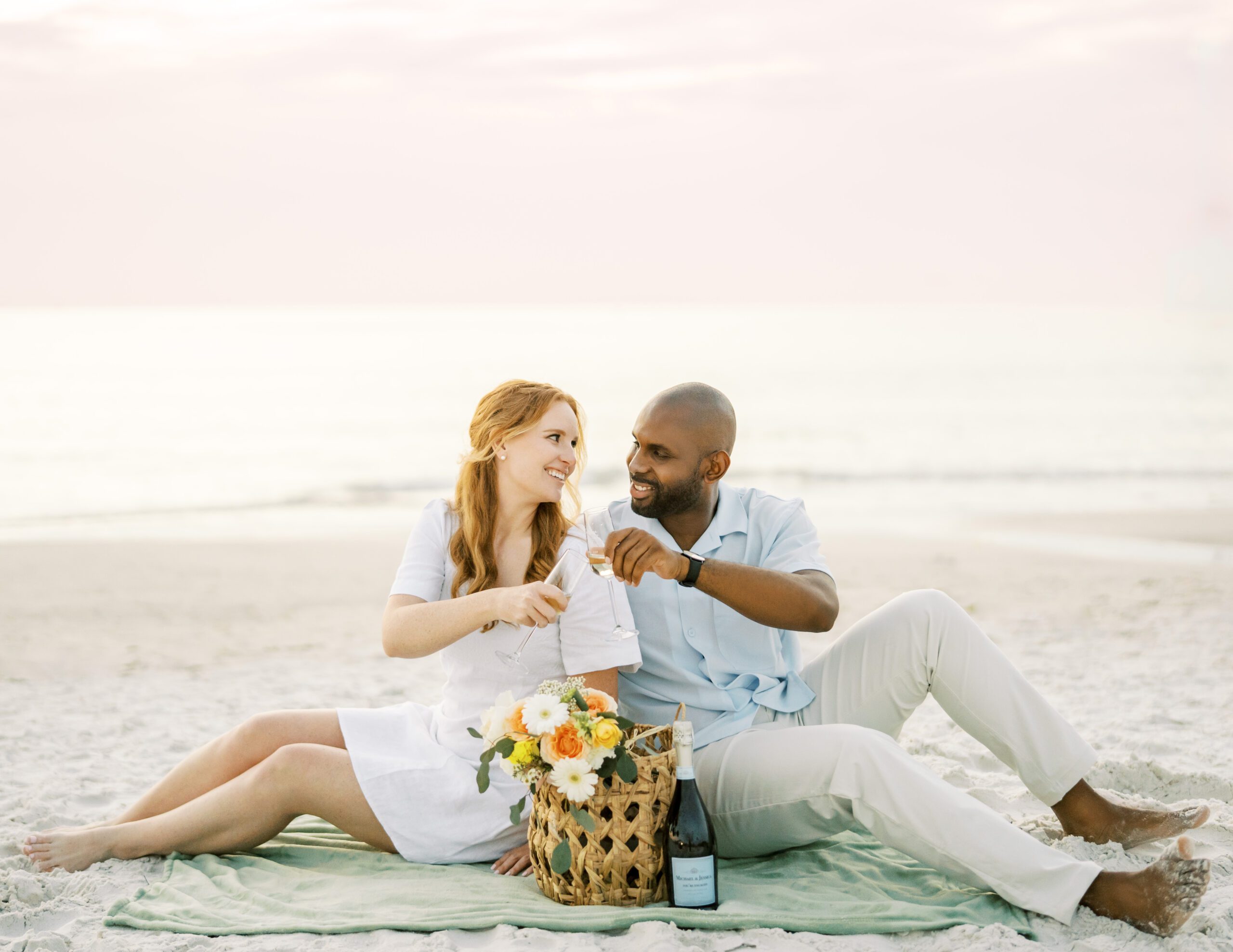 Fort de Soto beach engagement session man and woman toasting champagne in a picnic set up at the beach at sunset 